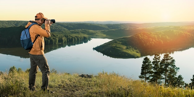 Fotógrafo de hombre con mochila y cámara tomando fotos de montañas al atardecer. Vacaciones de viaje de aventura de estilo de vida activo y saludable. Bandera.