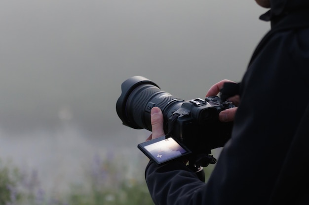 Foto fotógrafo irreconocible filmando una escena al aire libre con una cámara digital negra contemporánea en un trípode con pantalla abatible