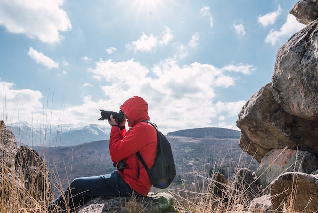 Fotógrafo irreconocible sentado tomando una foto del paisaje con montañas