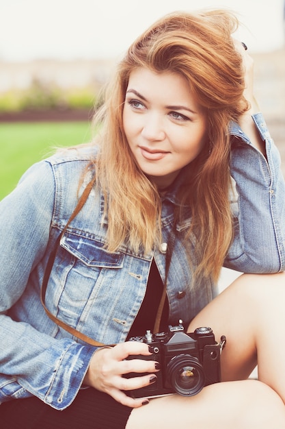 Fotógrafo joven caminando por la calle en una chaqueta de jeans con una vieja cámara