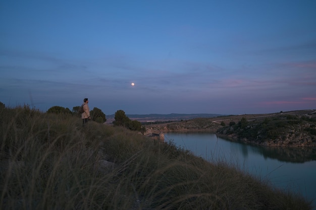 Fotógrafo latino com uma câmera tira fotos em uma lagoa e a lua ao anoitecer