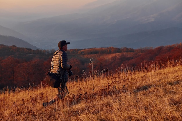 Fotógrafo masculino de pé e trabalhando na majestosa paisagem de árvores de outono e montanhas no horizonte