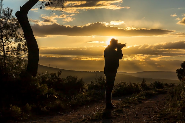 Foto fotógrafo masculino fotografando o pôr do sol em um dia com nuvens.