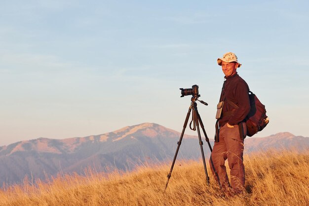 Fotógrafo masculino de pie y trabajando en el majestuoso paisaje de árboles y montañas de otoño en el horizonte