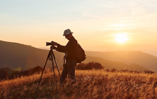 Fotógrafo masculino de pie y trabajando en el majestuoso paisaje de árboles y montañas de otoño en el horizonte