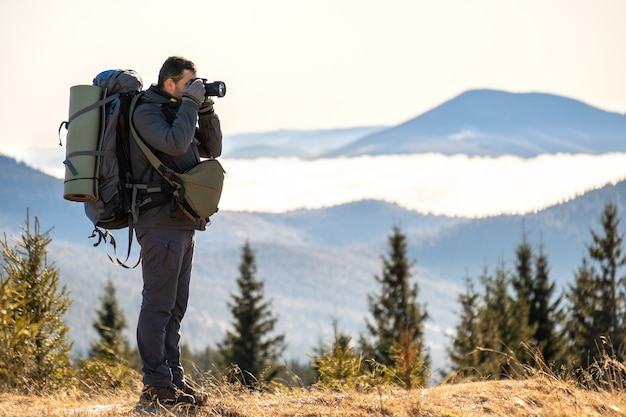 Fotógrafo con mochila de senderismo tomando fotografías de la naturaleza con cámara de fotos digital