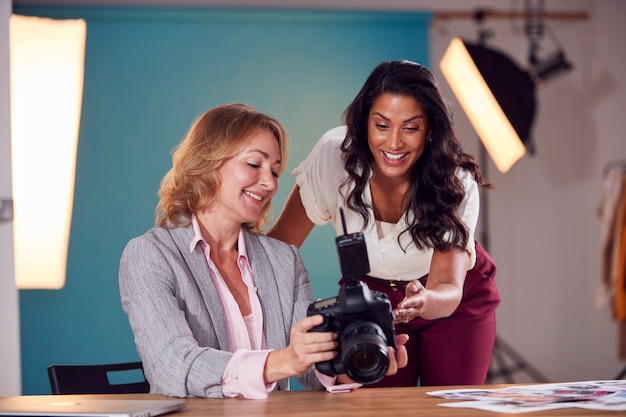 Fotógrafo de moda femenina madura con el cliente mirando imágenes de disparar en cámara en estudio