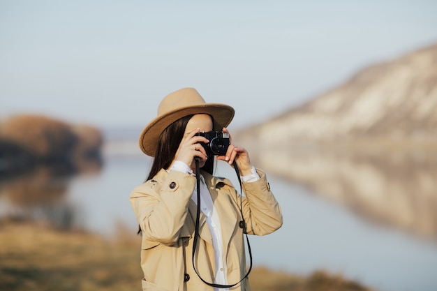 Fotógrafo de mujer en gabardina y sombrero tomando fotos en una cámara de película vintage