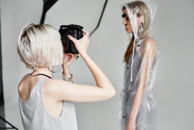 Fotógrafo de niña fotografiando modelo en capa transparente con máscara de granada en su rostro sobre fondo blanco en Studio