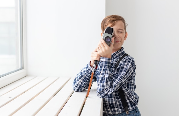 Fotógrafo, niños y concepto de hobby - lindo muchacho adolescente posando con cámara retro sobre fondo blanco.