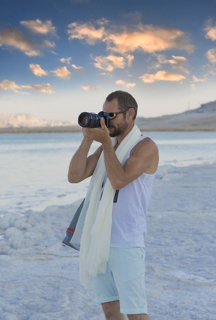 Fotógrafo de paisaje hombre tomando fotografías con cámara digital Viajes vacaciones trabajo y concepto de estilo de vida activo Hombre caucásico musculoso guapo usando imagen con cámara réflex digital en la playa