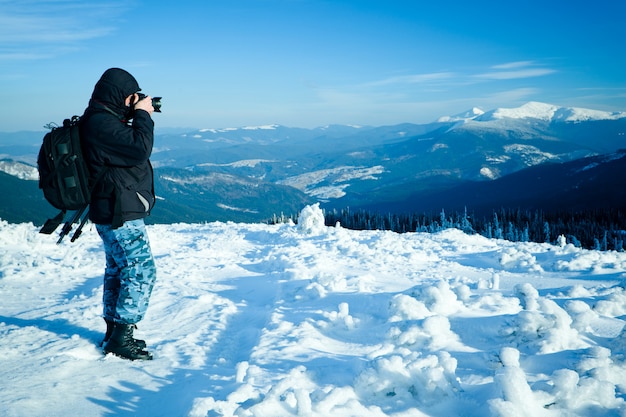 Fotógrafo de pie con cámara en la colina con vista panorámica del valle de invierno