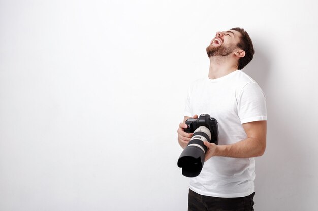 Fotógrafo profesional sonriente joven en camiseta blanca usa cámara digital con una lente larga