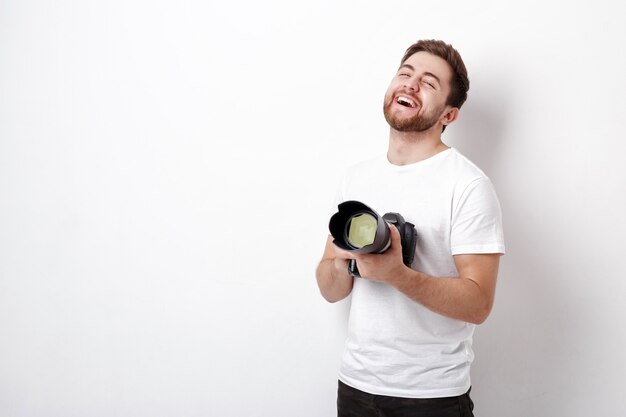 Fotógrafo profesional sonriente joven en camiseta blanca usa cámara digital con una lente larga