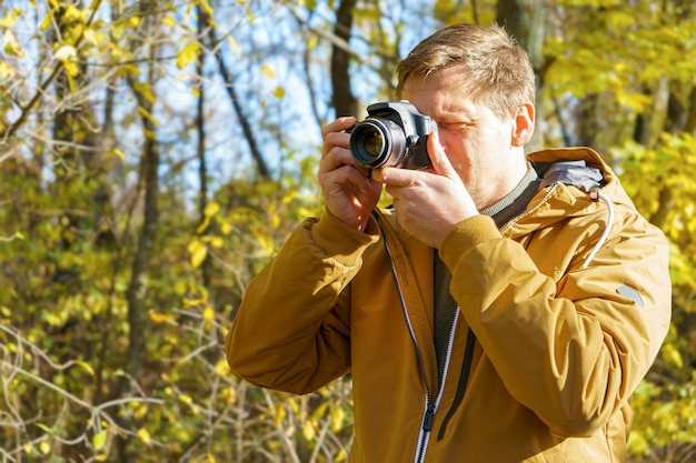 Fotógrafo profissional masculino fotografando ao ar livre na floresta amarela de outono
