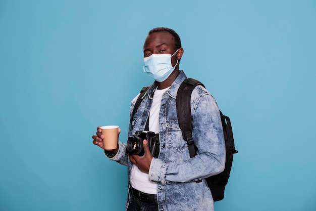 Fotógrafo profissional usando máscara facial de proteção contra vírus e com câmera enquanto viaja de férias. Homem com dispositivo DSLR e máscara protetora usando mochila enquanto aprecia a paisagem urbana.