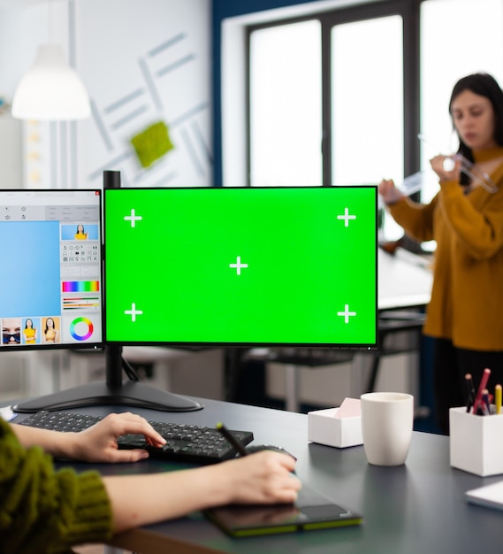 Fotógrafo que trabaja en una pantalla de maqueta verde, computadora con clave de croma, pantalla aislada mientras está sentado en el escritorio retocando el retrato de una mujer en un software de edición de fotos