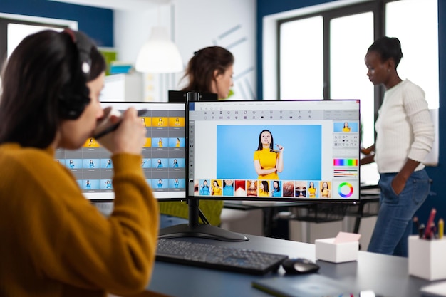 Fotógrafo retocador con auriculares retocando fotos usando lápiz óptico dibujando en tableta gráfica, trabajando en PC con dos pantallas. Editor de fotos Creator trabajando en la aplicación de software en la oficina de la agencia