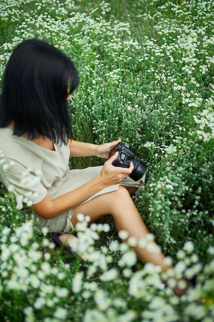 Fotógrafo de sexo femenino que se sienta al aire libre en el paisaje del campo de flor que sostiene una cámara, la mujer sostiene la cámara digital en sus manos. Fotografía de naturaleza de viajes, espacio para texto, vista superior.