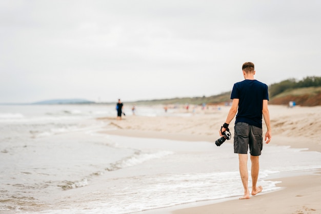 Fotógrafo solitario con una cámara en la mano caminando por la playa de verano