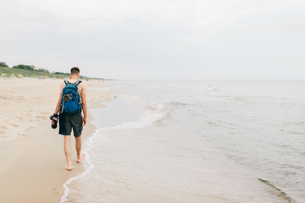 Fotógrafo solitário com uma câmera na mão, caminhando na praia