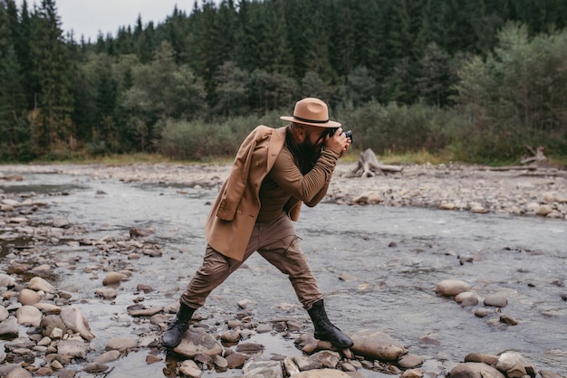 Fotógrafo tira fotos nas montanhas pedestre em pé nas rochas do rio com uma câmera profissional nas mãos com uma vista pitoresca no fundo