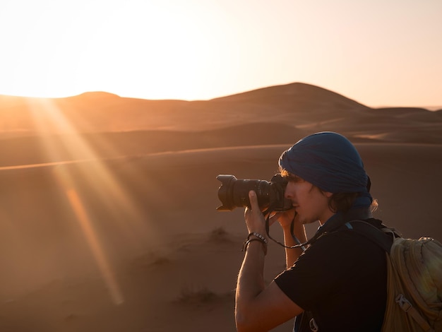 Fotógrafo tirando fotos do pôr-do-sol sobre dunas de areia no deserto de Merzouga, Marrocos