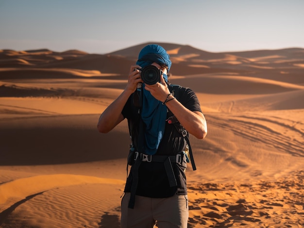 Fotógrafo tirando fotos no ensolarado deserto de Merzouga durante uma viagem a Marrocos