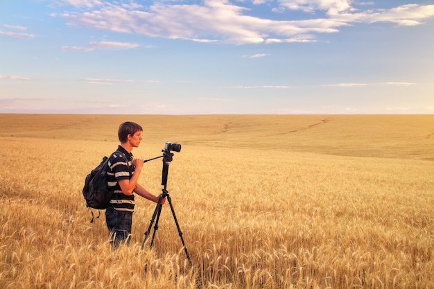 El fotógrafo toma fotografías en un campo de trigo. El hombre de la cámara en un campo al atardecer. Hombre trabajando en la naturaleza.