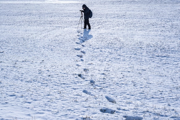 El fotógrafo con un trípode en un campo nevado toma fotografías de huellas de paisajes en la nieve