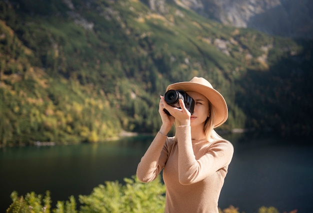 Fotógrafo turista viajante em pé no topo da montanha segurando nas mãos câmera de fotos digitais