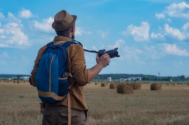 Fotógrafo viajante com uma câmera na mão no contexto de um campo e palheiros