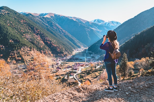 Fotógrafo viajero de moda hipster mujer con estilo en un sombrero de fieltro con mochila marrón tomando fotos de las montañas y el lago uzungol en Trabzon durante el viaje a Turquía