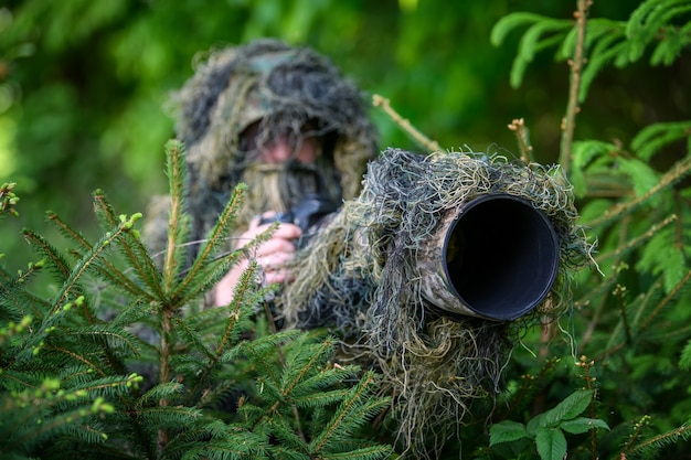 Fotógrafo de vida silvestre en el traje de camuflaje ghillie de verano trabajando en la naturaleza