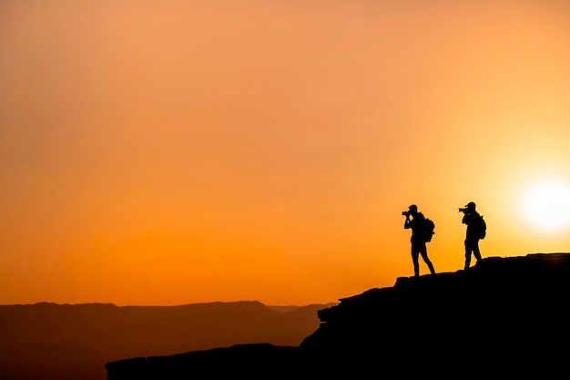 Fotógrafos de silhuetas que fotografam um pôr do sol nas montanhas. Conceito de fotógrafo