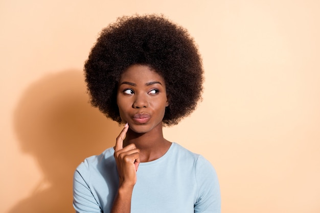 Fotoporträt einer afroamerikanischen Frau, die denkt, das Kinngesicht mit einem Finger zu berühren, isoliert auf pastellbeigem Hintergrund