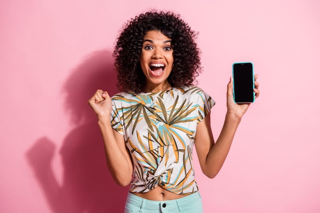 Fotoporträt einer feiernden Frau, die Telefon mit Leerzeichen in einer Hand hält, isoliert auf pastellrosafarbenem Hintergrund