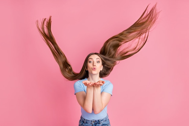 Fotoporträt einer Frau mit fliegenden Haaren, die einen Luftkuss mit beiden Händen nach oben sendet, isoliert auf pastellrosafarbenem Hintergrund