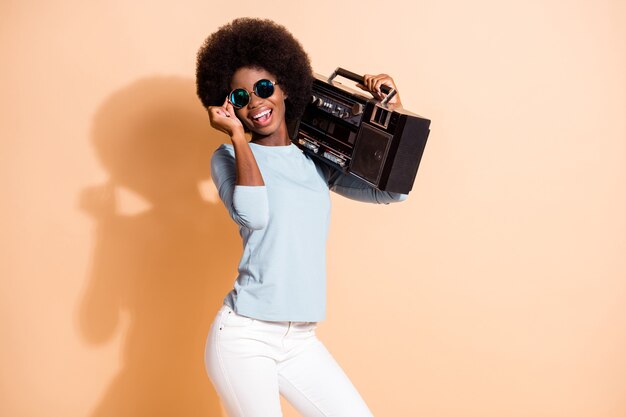 Fotoporträt eines afroamerikanischen Mädchens, das eine Boombox-Brille hält, die auf pastellbeigem Hintergrund isoliert ist?