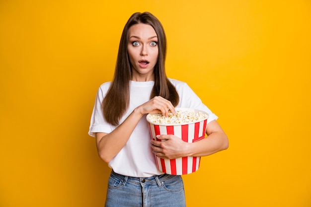 Fotoporträt eines erstaunten Mädchens, das Karton mit Popcorn hält und Blockbuster sieht, isoliert hellgelber Farbhintergrund