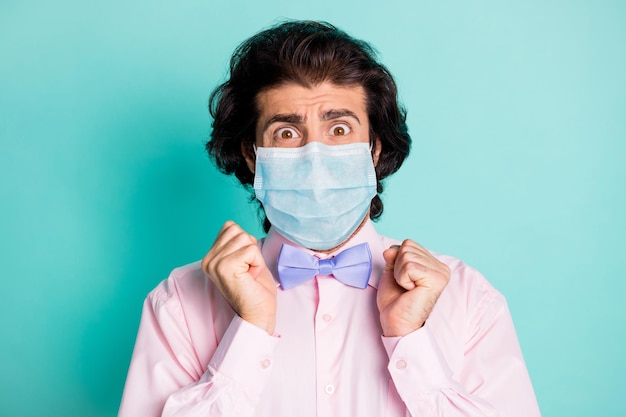 Fotoporträt eines verängstigten Mannes, der eine medizinische Maske trägt, die auf pastelltürkisfarbenem Hintergrund isoliert ist?