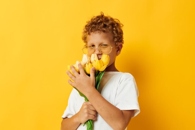 Fotoporträt gelockter kleiner Junge, der einen Blumenstrauß hält, ein Geschenk gelber Hintergrund unverändert