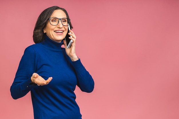 Fotoporträt von schockiert erstaunt überrascht senior reife gealterte Frau, die Handy hält und verrückte Rabatte sieht, die lässig auf rosafarbenem Hintergrund tragen.