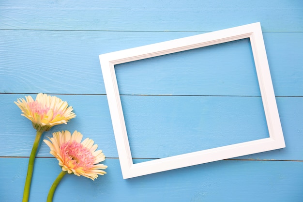 Fotorahmen und gelbe Blume auf hellem blauem hölzernem Hintergrund mit den Blumenblättern. Sommerwohnung lag.