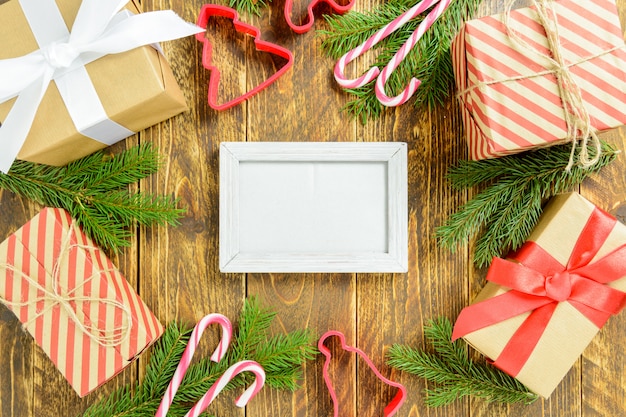 Fotorahmen zwischen Weihnachtsdekoration, mit Geschenkboxen und Zuckerstange auf einem braunen Holztisch. Draufsicht, Feld, zum des Raumes zu kopieren.