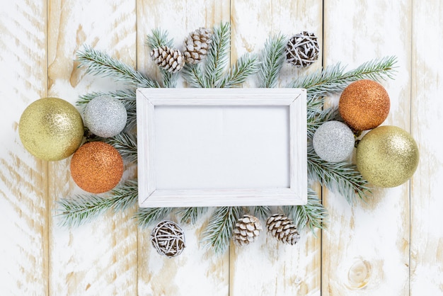 Fotorahmen zwischen Weihnachtsdekoration, mit mehrfarbigen Bällen und Kiefernkegeln auf einem weißen Holztisch. Draufsicht, Feld, zum des Raumes zu kopieren