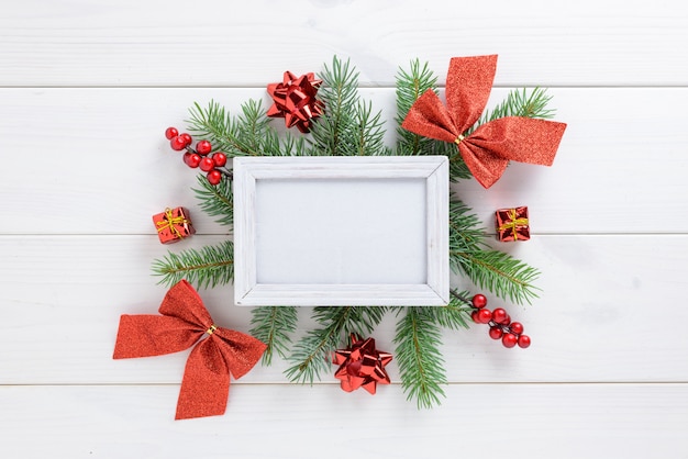 Fotorahmen zwischen Weihnachtsdekoration, mit rotem Bandbogen auf einem weißen Holztisch. Draufsicht, Feld, zum des Raumes zu kopieren