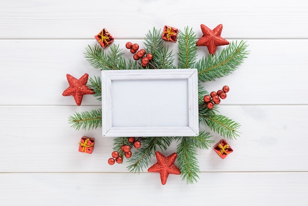 Fotorahmen zwischen Weihnachtsdekoration, mit roten Sternen und Geschenkbox auf einem weißen Holztisch. Draufsicht, Feld, zum des Raumes zu kopieren