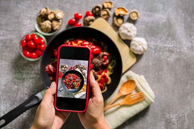 Fotos Suche nach imMachen Sie ein Foto von Spaghetti mit einem MobiltelefonDraufsicht einer Frau beim Fotografieren