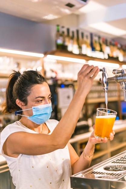 Fotosession mit einer Kellnerin mit einer Gesichtsmaske in einer Bar. Ein kaltes Bier trinken